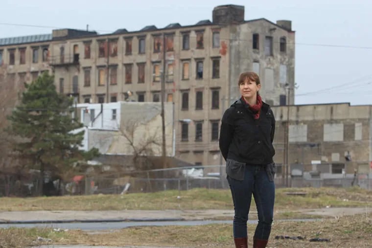 Artist Maria Moller has completed a survey of the "mega lots", the local name for an area of vacant land in East Kensington that now stretches almost 4 blocks.  She stands in the vacant lot where the Providence Dye Works once stood on April 2, 2014.  In the background is one of the few industrial buildings still standing. These parcels, all razed by factory fires, have been a drag on the neighborhood, but also present opportunities for development, open space and catalyzing change. ( CHARLES FOX / Staff Photographer )