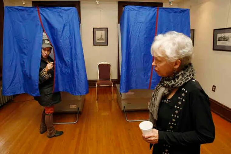 Elizabeth Sachs peeps out from a voting machine at the Media Borough Hall to ask a question, while Joye Asta, a machine inspector, keeps an eye on the equipment.