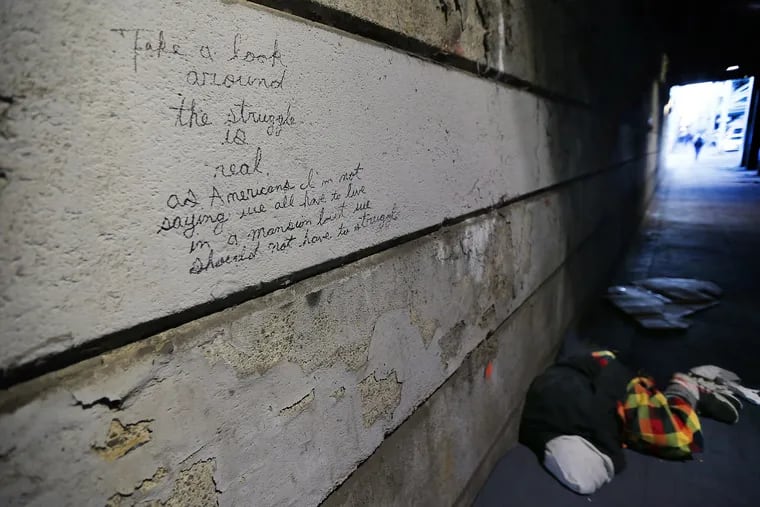 A homeless man sleeps under a handwritten message that reads: "Take a look around the struggle is real. as Americans I'm not saying we have to live in a mansion but we should not have to struggle," under the bridge at Kensington and Lehigh. City officials have worked to get Philadelphia's rising homeless population into housing, but because of the opioid crisis, deaths among people experiencing homelessness are increasing.