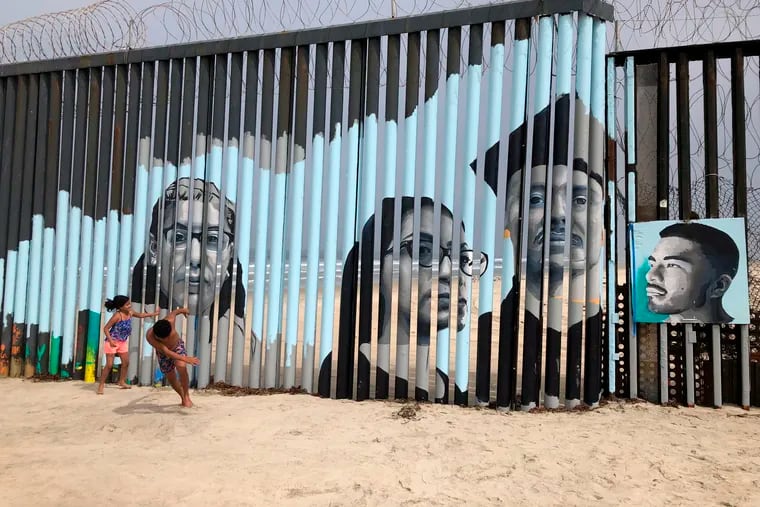 Children play in front of a new mural on the Mexican side of a border wall in Tijuana, Mexico Friday, Aug. 9, 2019. The mural shows faces of people deported from the U.S. with barcodes that activate first-person narratives on visitors' phones. Lizbeth De La Cruz Santana conceived the interactive mural in Tijuana as part of doctoral dissertation at the University of California, Davis. (AP Photo/Elliot Spagat)