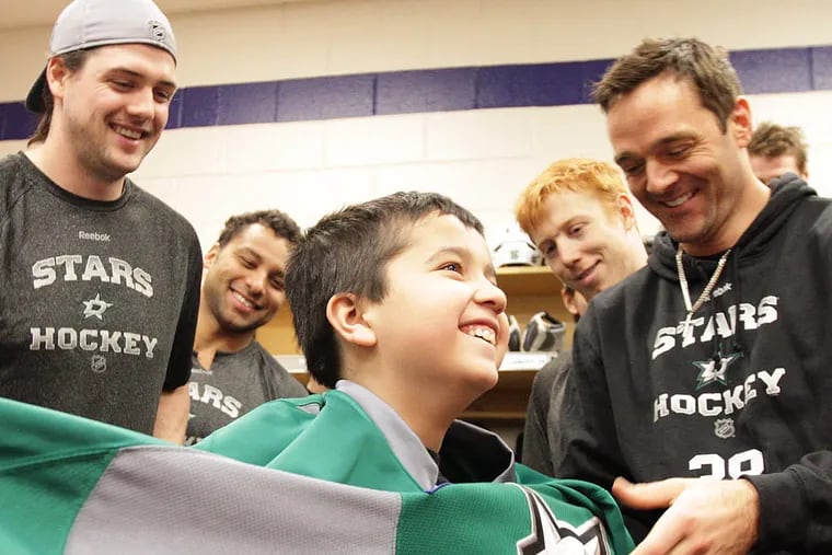 TJ Ramos, center, who suffered a heart attack and was diagnosed with CPVT, laughs as members of the Dallas Stars put a team jersey on him at the Wells Fargo Center in Philadelphia on March 20, 2014. Dallas Star player, Rich Peverley, also has CPVT.  Ramos is a Flyers fan. ( DAVID MAIALETTI / Staff Photographer )
