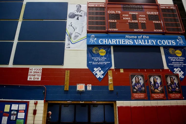 Tim McConnell, the high school basketball coach for Chartiers Valley, peeks out while pushing a button to lower the gym's basketball hoops underneath a banner of his son, 76ers point guard T.J. McConnell, from when he played in college at Arizona, that hangs next to the scoreboard.
