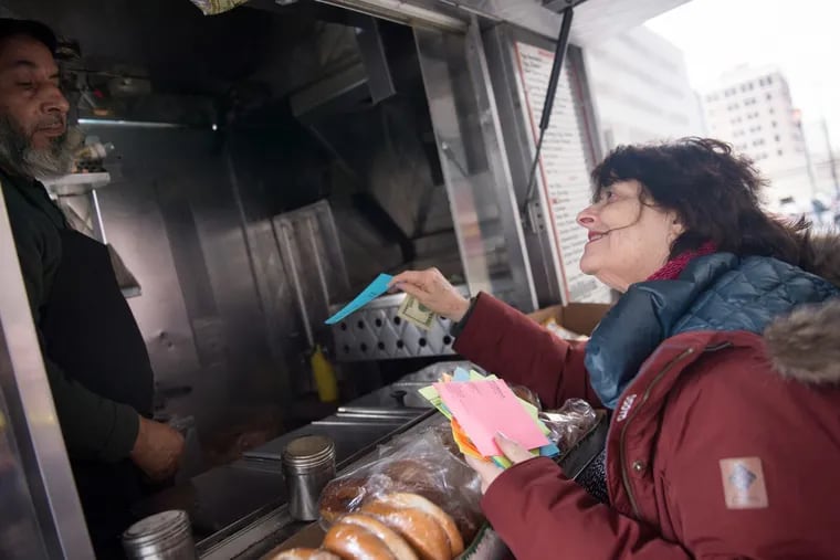 Nina Schafer, right, offers a poem to Mohammad Ali, a food truck vendor in Center City April 10, 2018. Schafer hands out about 12,000 poems each year to people with whom she interacts.
