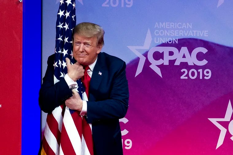 President Donald Trump hugs the American flag as he arrives to speak at Conservative Political Action Conference in Oxon Hill, Md., March 2, 2019. The President promised an executive order to protect campus free speech.