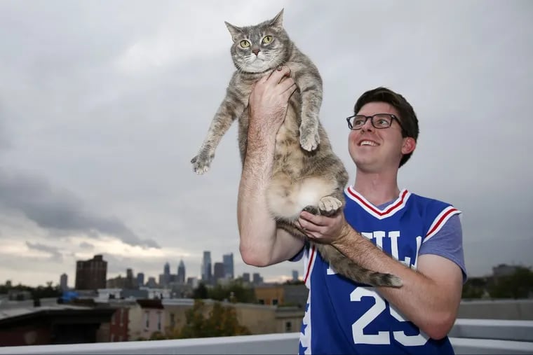 Sixers fan Dennis Grove raising his cat Izzy on deck outside their North Philadelphia home on Monday.