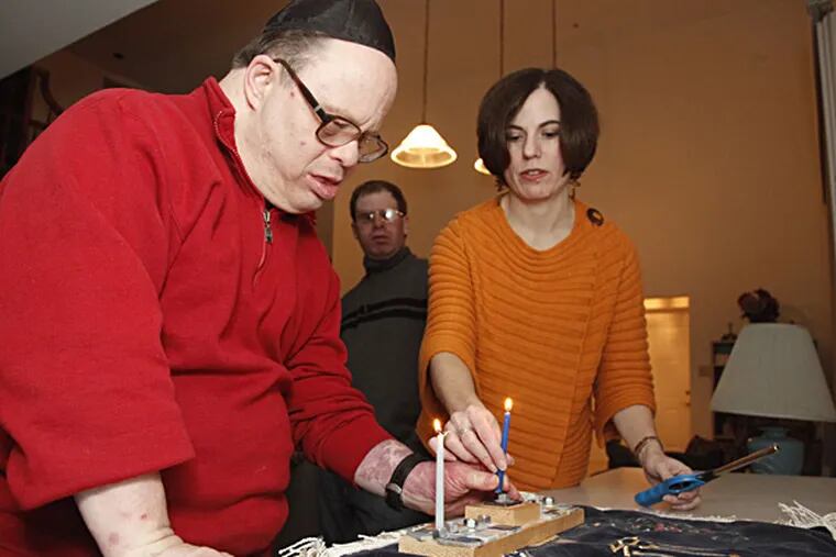 Doug Jarett and Stacy Jarett Levitan light the candles for the first night of Hanukkah at the Strauss/Actman group home in Wynnewood. RYAN S. GREENBERG / Staff Photographer