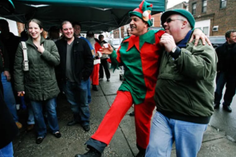 Ray the Elf dances with Vinny Roth outside Isgro Pastries. This year, Ray Verbrugghe and Tony Ciaccio Sr. led a band of 20 merry men on a bus trip from the suburbs into the Italian Market for the soggy pre-Christmas revelry.