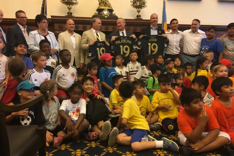 Mayor Kenney (center) poses with Eastern Pennsylvania Youth Soccer CEO Chris Branscome (left), Philadelphia Union Foundation executive director Paul Howard, and dozens of youth soccer players from across the city at a news conference announcing the construction of 15 mini-pitches and two full-sized soccer fields in Philadelphia over the next five years.