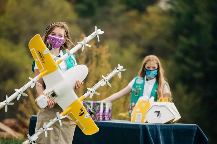 In this April 14, 2021 image provided by Wing LLC., Girl Scouts Alice, right, and Gracie pose with a Wing delivery drone in Christiansburg, Va. The company is testing drone delivery of Girl Scout cookies in the area. (Sam Dean/ Wing LLC via AP)