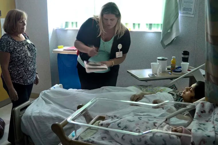 Story Storks volunteers Maureen Hicks (left) and Adrienne Evans visit Neema Bhat and her day-old daughter, Veeksha Dixit, at Cooper University Hospital. Reading to an infant &quot;is about making a connection,&quot; Evans says of their program. TOM GRALISH / Staff Photographer