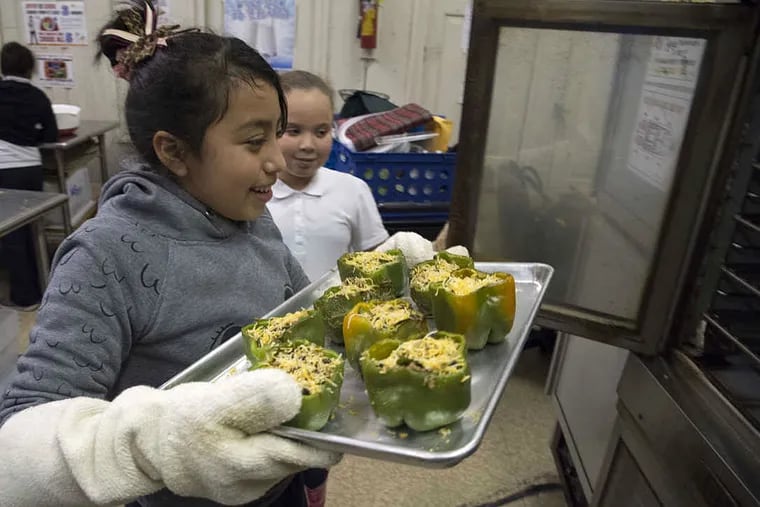 McClure Elementary School fifth grader Karen Godinez carries stuffed peppers to the oven as classmate Briannalyss Santiago opens the oven door as part of the My Daughter’s Kitchen program.