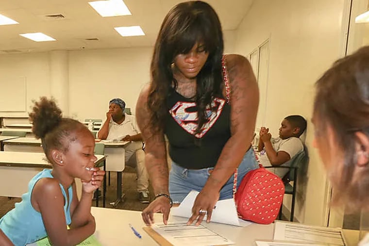 Volunteer Andrea Foster (right) helps Saveena Branch (center) fill out paperwork at school district HQ as Branch’s daughter Rashaia Robertson looks on..