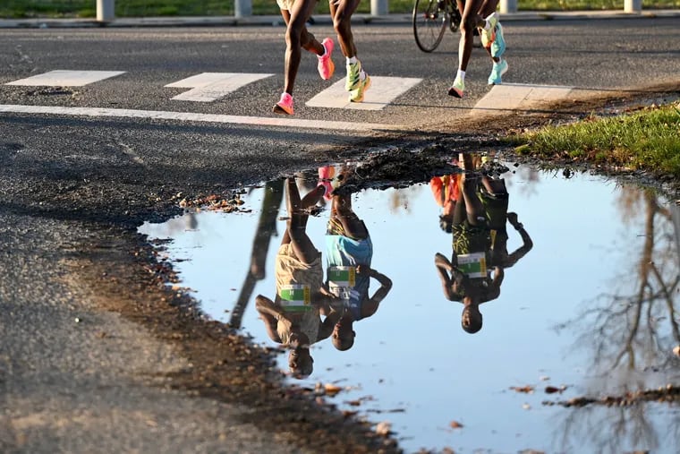 November 20, 2023: The pack-leading group of elite runners are reflected in a puddle as the 30th annual Philadelphia Marathon travels through Fairmount Park.