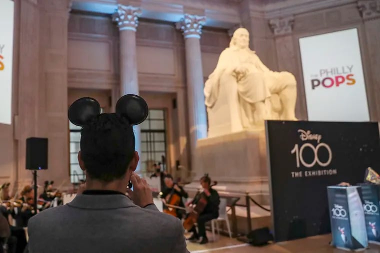 Guests wear Mickey Mouse ears while the Philly Pops performs inside of Benjamin Franklin National Memorial Hall at the Franklin Institute before the start of the news conference introducing "Disney100: The Exhibition."