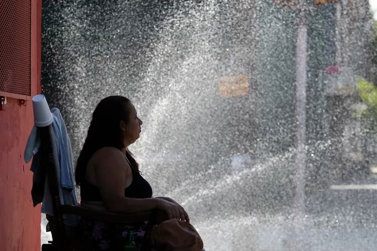 A woman sits in the mist of a spraying fire hydrant to keep cool at 5th and Dauphin Streets on July 18 2020.