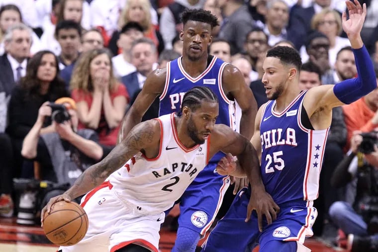 Jimmy Butler, left, and Ben Simmons, right, of the SIxers converge upon Kawhi Leonard of the Raptors during the 2nd half of their NBA playoff game at the Scotiabank Arena in Toronto on April 29, 2019.