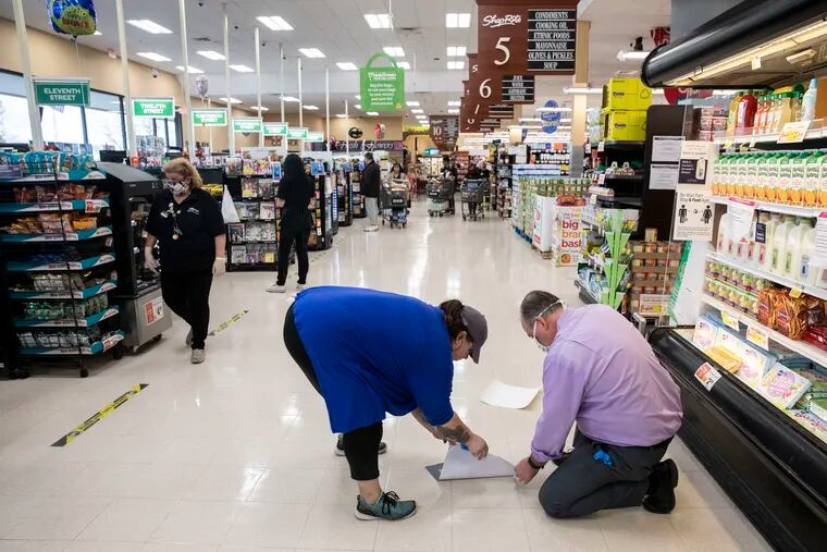 Kate Jacobi, from Mural Arts Philadelphia, and John Coyle, store manager, install spacing decals as a part of the Space Pad Project at the Shop Rite on West Oregon Avenue in South Philadelphia, Pa. on Friday, April 3.
