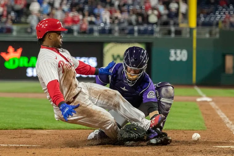 Jean Segura  of the Phillies scores in the fourth inning on a base hit by Rhys Hoskins as the ball gets away from Dom Nuñez of the Rockies.
