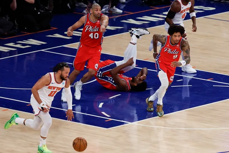 Sixers center Joel Embiid lays on the floor holding his knee as New York Knicks guard Jalen Brunson dribbles the basketball in Game 1 of the first round of the NBA Eastern Conference playoffs on April 20.