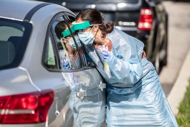 Healthcare worker Maria Newcomb leans in over the passenger seat to administer a coronavirus test to a man in his car.