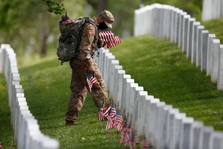 A member of the 3rd U.S. Infantry Regiment, also known as the Old Guard, wears a face mask as he places flags in front of each headstone for "Flags-In" at Arlington National Cemetery in Arlington, Va., Thursday, May 21, 2020, to honor the nation's fallen military heroes ahead of Memorial Day.