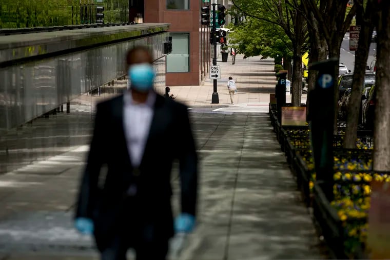 A man wearing a mask and gloves walks along the corner of 18th Street and K Street in Northwest, an area usually packed with people this time of day, Wednesday, April 29, 2020, in Washington.