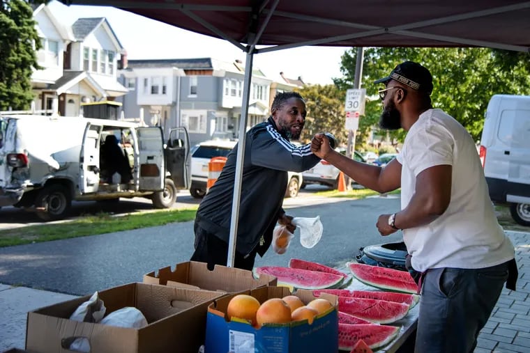 Abdul Jabar (right) fist bumps regular customer Anthony Coprich at his Soul Glo Healthy Lifestyle produce stand on Cobbs Creek Parkway in West Philly.
