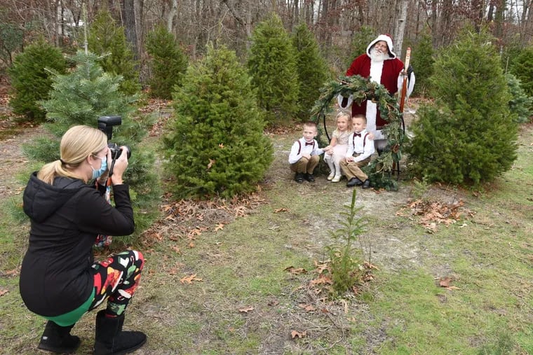 At Triple Dog Dare Ya Christmas Tree Farm in Franklinville, N.J., photographer Colleen Kuzniasz takes pictues of (from left) Keegan, Karlee, and Karson Whelan as Santa Kringle (Frank Naimoli) holds his distance behind them.