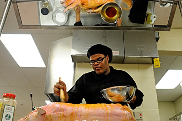 Junior Antony Knox is reflected in an overhead mirror as he seasons a pig with a spice rub for roasting. The food festival will be at the Westampton campus on Woodlane Road from 7 to 10 p.m. TOM GRALISH / Staff Photographer