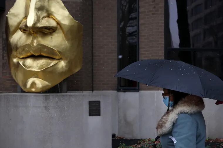 A pedestrian past the "Face Fragment" statue by Arlene Love outside the Monell Chemical Senses Center in West Philadelphia on Wednesday. Light snow has spread across the region, leaving a coating in some areas to well to the north and west of the city, but Philadelphia will likely still be waiting for its first official measurable snowfall of the season.