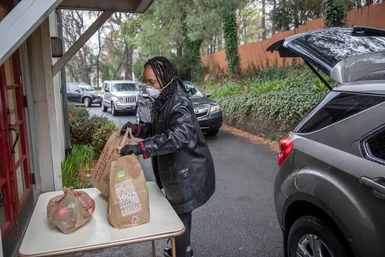 A person wearing a surgical mask picks up the bags of food left on the distribution table at the Jenkintown Food Cupboard.