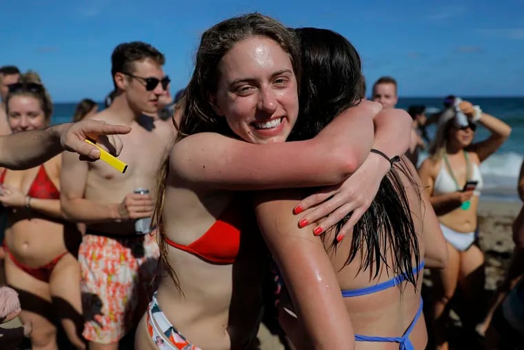 Two spring break revelers hug while partying in a large crowd on the beach, Tuesday, March 17, 2020, in Pompano Beach, Fla. As a response to the coronavirus pandemic, Florida Gov. Ron DeSantis ordered all bars be shut down for 30 days beginning at 5 p.m., and many Florida beaches are turning away spring break crowds, urging them to engage in social distancing.