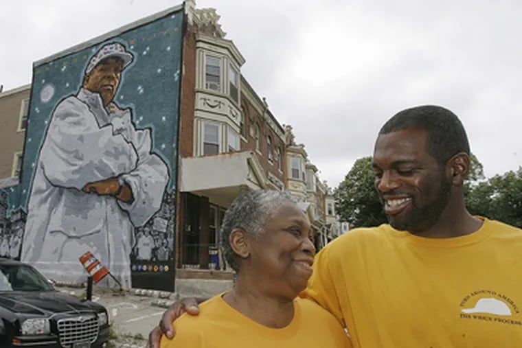The Herman Wrice mural at 34th and Spring Garden Streets is about to be covered up by development. “The mural is not just a picture of a man,” says Wrice’s widow, Jean, here with son Tony. “It’s a picture of a movement.” (Akira Suwa / Staff Photographer)