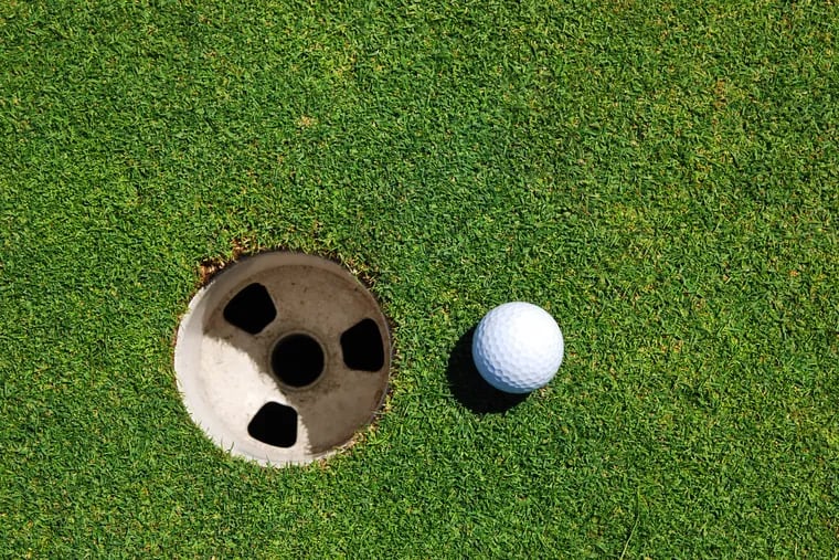 A golf ball rests two inches from a hole.