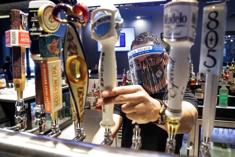 A bartender pours a beer while wearing a mask and face shield amid the coronavirus pandemic at Slater's 50/50 Wednesday, July 1, 2020, in Santa Clarita, Calif. According to a new poll, Americans overwhelmingly are in favor of requiring people to wear masks around other people outside their homes, reflecting fresh alarm over spiking infection rates. The poll also shows increasing disapproval of the federal government's response to the pandemic.