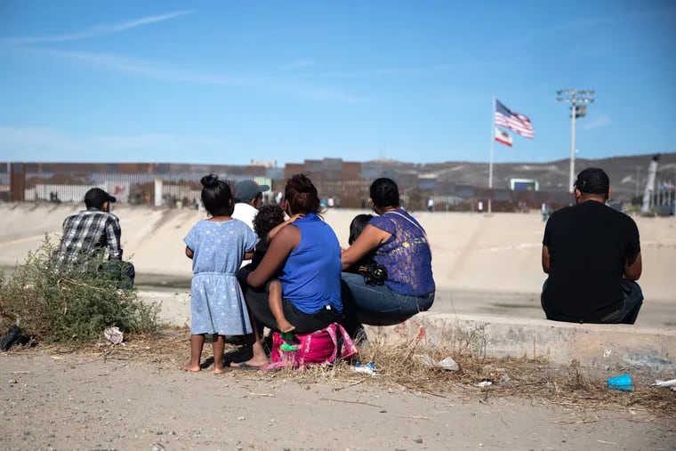 Central American migrants sit along the Tijuana River as an American flag flies near the U.S. and Mexico border in Tijuana, Mexico, in November.