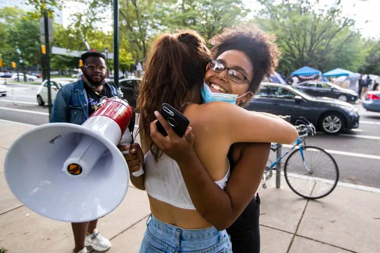 Organizer Dominique McQuade (right) gets hugged by Malia Paulmier after McQuade announced through the bullhorn that the encampments would stay at least until a federal judge would decide on an injunction Tuesday or Wednesday.