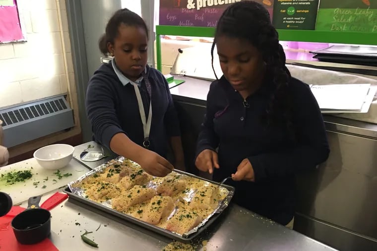Malaan McCrea, left, sprinkles fresh chopped parsley on the cod, while Miracle Brown presses the breadcrumbs into the fish during the My Daughter's Kitchen after school cooking class at James Lowell Elementary School in North Philadelphia.