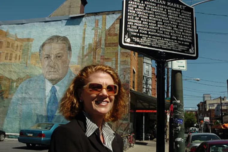 Celeste Morello poses on South 9th Street near a new marker commemorating the Italian Market. She designed the marker. A book she authored - "The Philadelphia Italian Market Cookbook: The Taste of South 9th Street," was sold down the street until recently. (Sarah J. Glover / Inquirer)