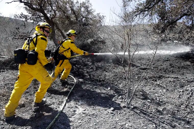Brett Palmer (left) and Anthony Ayala with the South Placer Fire Department hose down a hot spot from a wildfire Saturday, Oct. 12, 2019, in Porter Ranch, Calif.