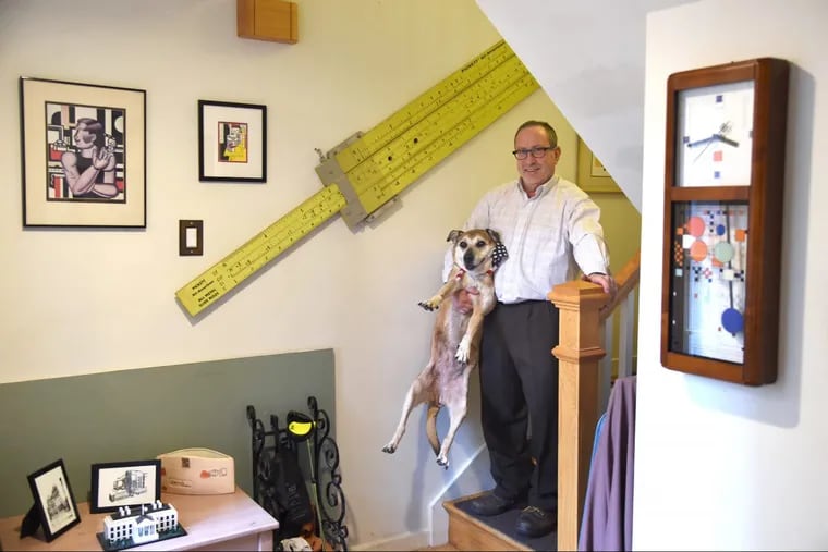 Retired teacher Jerry Silverman, here with his 17-year-old dog Shayna Punim, has decorated his remodeled South Philadelphia home with collectibles, such as the giant classroom demonstration slide rule on the staircase wall.