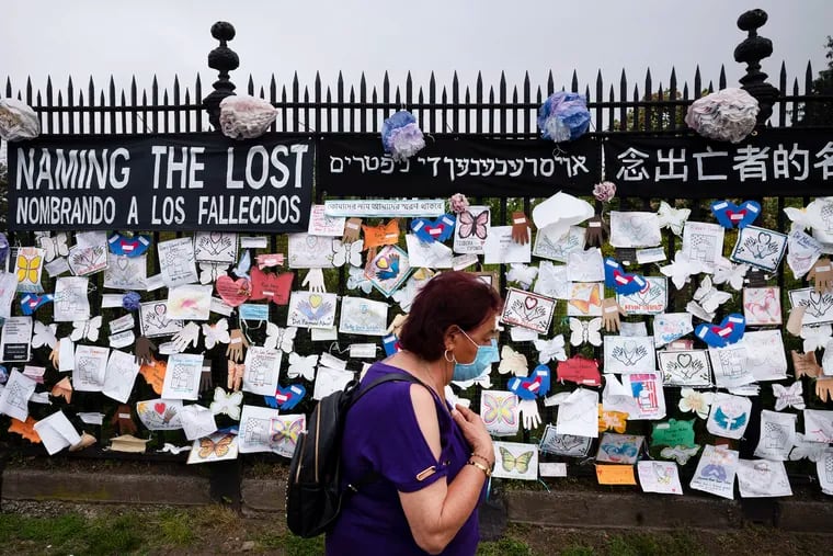 A woman passes a fence outside Brooklyn's Green-Wood Cemetery adorned with tributes to victims of COVID-19 on May 28, in New York. The memorial is part of the Naming the Lost project, which attempts to humanize the victims who are often just listed as statistics.