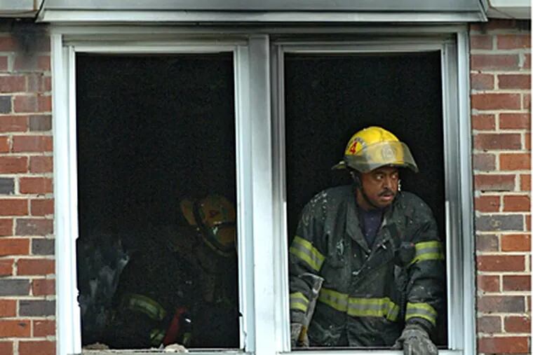 A firefighter leans out of a second-story window of a Southwest Philadelphia home where a 12-year-old boy died in an early morning fire.  ( Clem Murray / Staff Photographer )