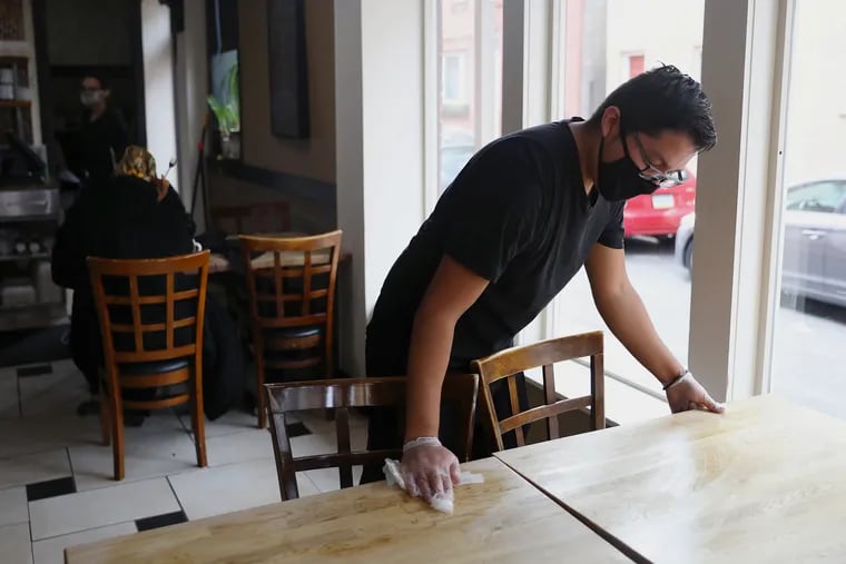 Busboy Luis Sandoval uses a disinfecting wipe to clean off a table at Green Eggs Cafe on Dickinson Street in South Philadelphia. Restaurants have grown increasingly desperate for workers as pandemic restrictions ease.