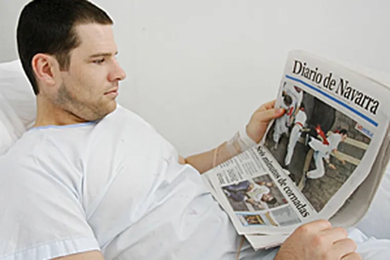 Michael Lenahan, 23, of Philadelphia, Pa. lies on a hospital bed as he looks at the front page of a newspaper showing the moment that he was gored by a fighting bull during a traditional bull run in Pamplona, Spain, Friday July 13, 2007. His brother was also gored.
