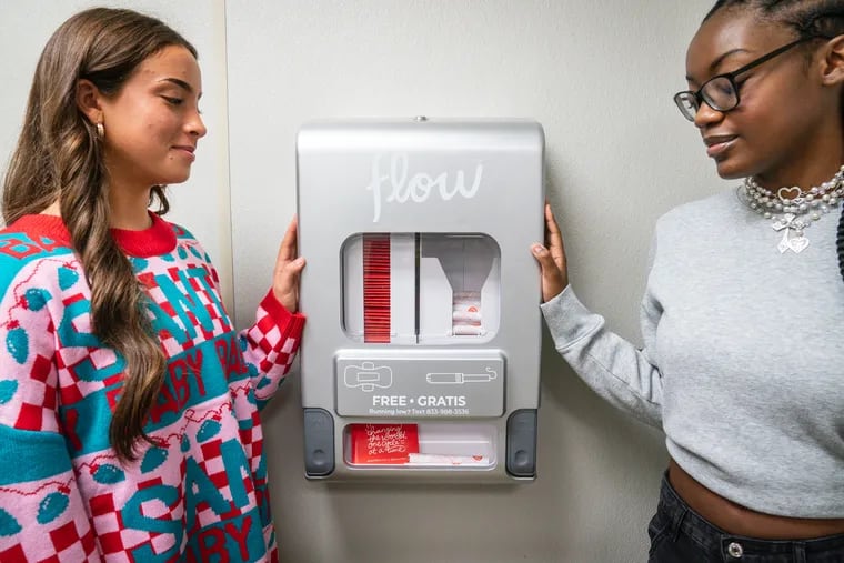 Students Macie Madden, left, and Gabrielle Clement, right, demonstrate how the free period products dispenser works at Haddon Heights High School.