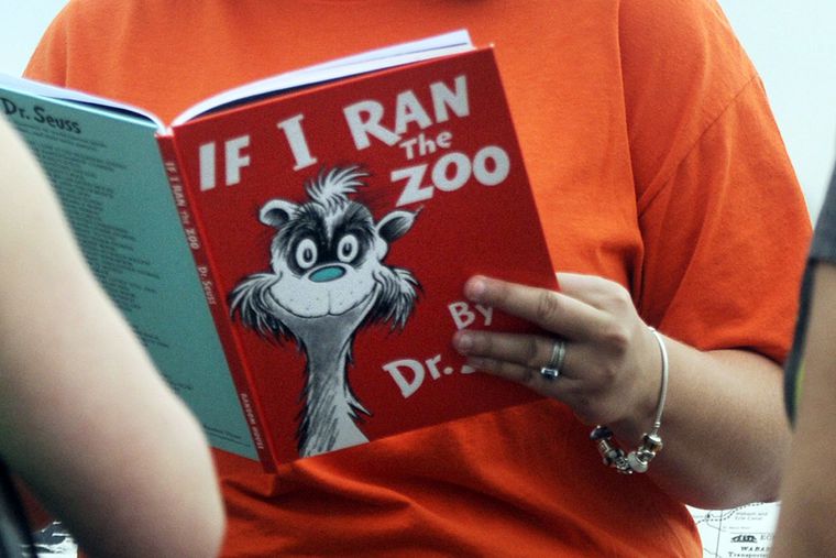 In this Sept. 24, 2013, file photo, Courtney Keating, education coordinator of The Literacy Center in Evansville, Ind., reads "If I Ran the Zoo," By Dr. Seuss, to passersby during an event to promote literacy. Dr. Seuss Enterprises, the business that preserves and protects the author and illustrator's legacy, announced on Tuesday, March 2, 2021, that it would cease publication of several children's titles including "And to Think That I Saw It on Mulberry Street" and "If I Ran the Zoo," because of insensitive and racist imagery.