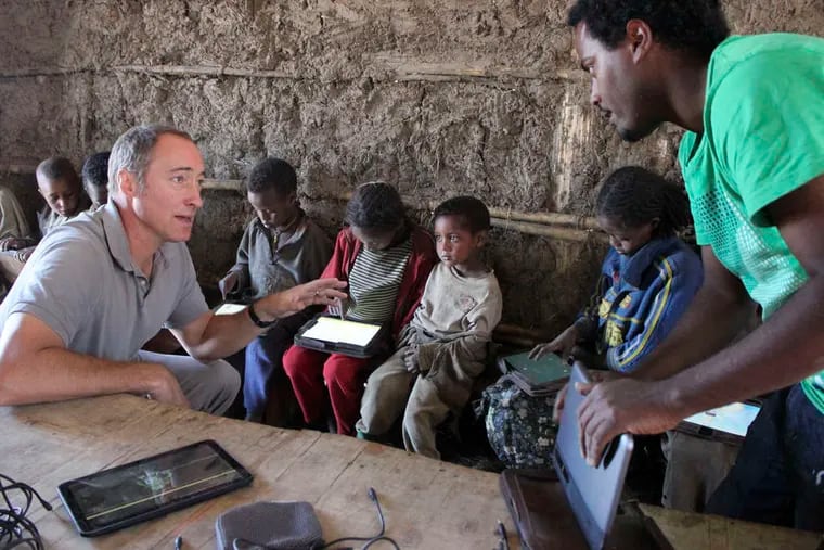 As children in the village of Wenchi use their computer tablets, Matt Keller (left) who is in charge of the One LaptopPer Child project in Ethiopia, speaks with program technician Michael Girma.