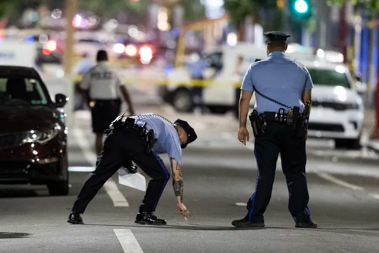 Philadelphia police officers make chalk marks on the street at the scene of a mass shooting at Second and South Streets Saturday night that left three dead and 11 wounded.