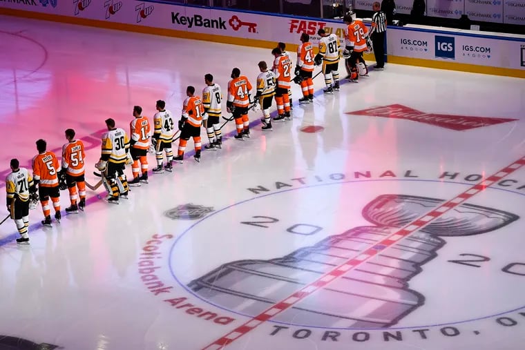Flyers and Penguins players line up together for the national anthems before Tuesday's exhibition game in Toronto.